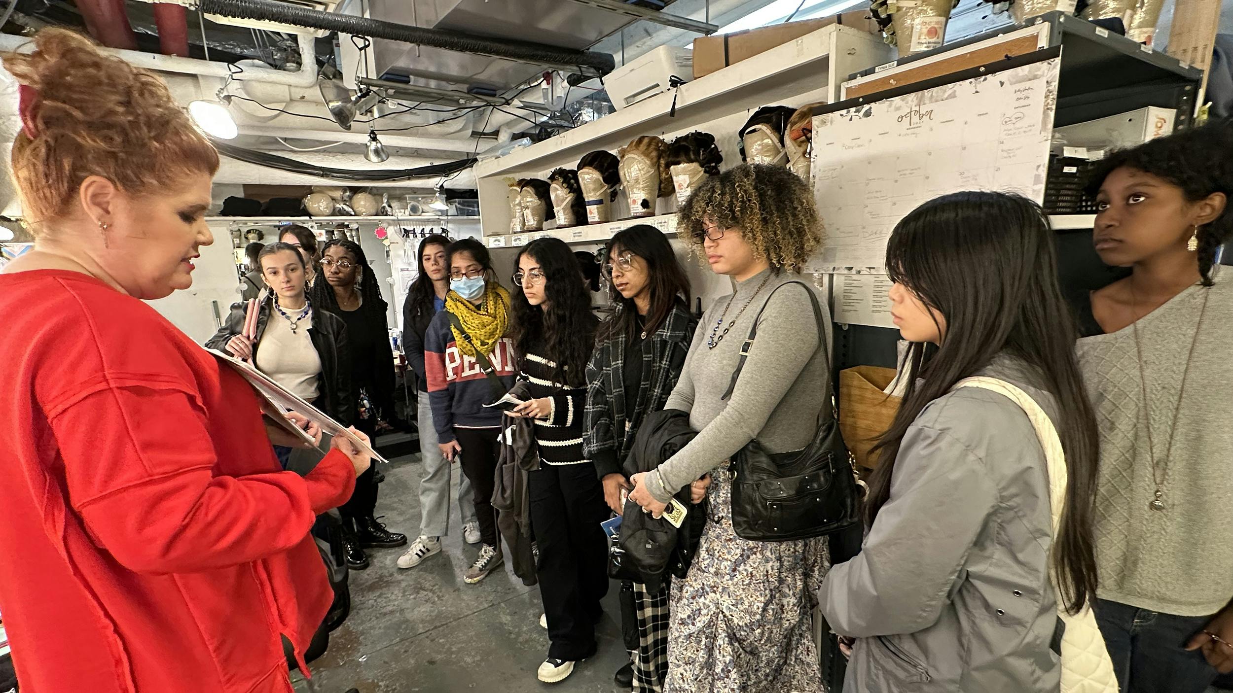 Students during a backstage tour of SO<E LIKE IT HOT on Broadway: a group of high school girls and non-binary students tour the Wig Room backstage at SOME LIKE IT HOT on Broadway.
